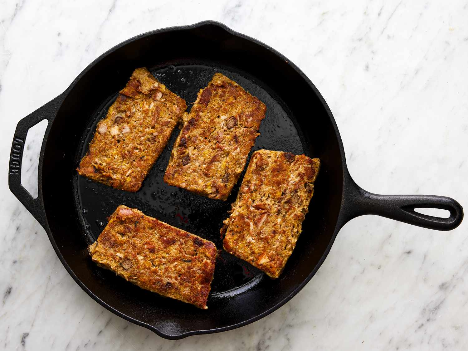 Overhead view of slabs of scrapple frying in a cast iron pan