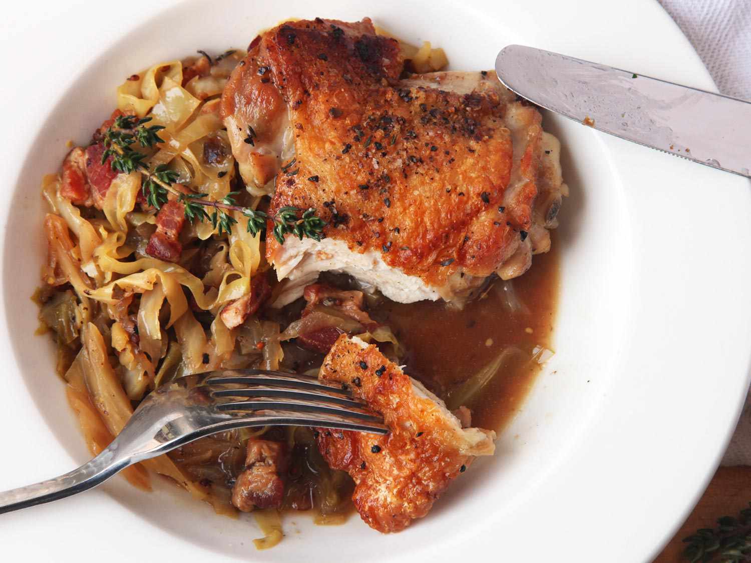 Fork piercing a bite of crispy braised chicken thigh from plate