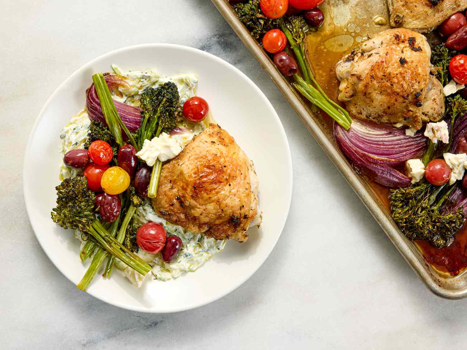 Roasted chicken thigh served with vegetables including broccolini cherry tomatoes and onions with a creamy sauce on the side