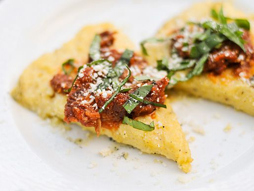 Closeup of grilled polenta, cut into wedges and topped with marinara, basil, and parmesan.