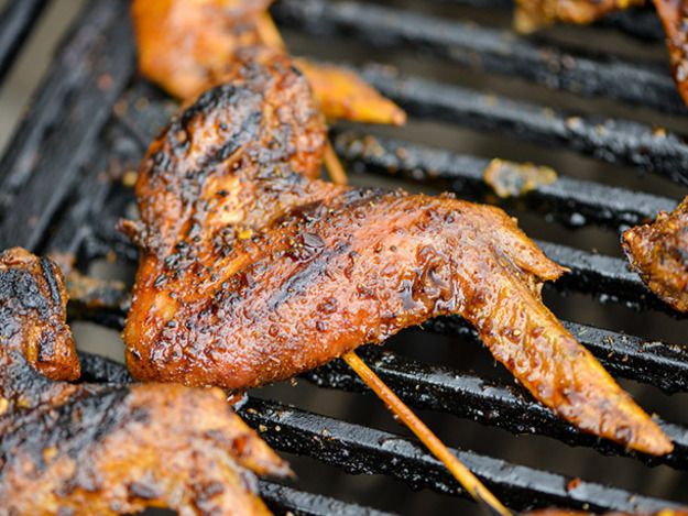 A charred, sauce-coated chicken wing with a skewer inserted into it, resting on a grill.