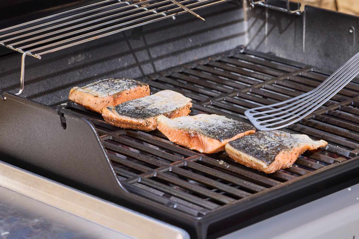 A spatula hovering over salmon cooking on the Weber Spirit E-210 Gas Grill