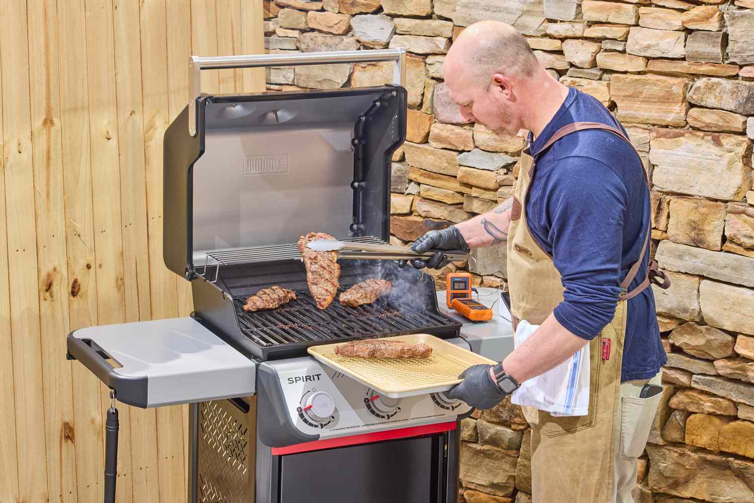 A person using tongs to move steaks from the Weber Spirit E-310 Gas Grill onto a tray