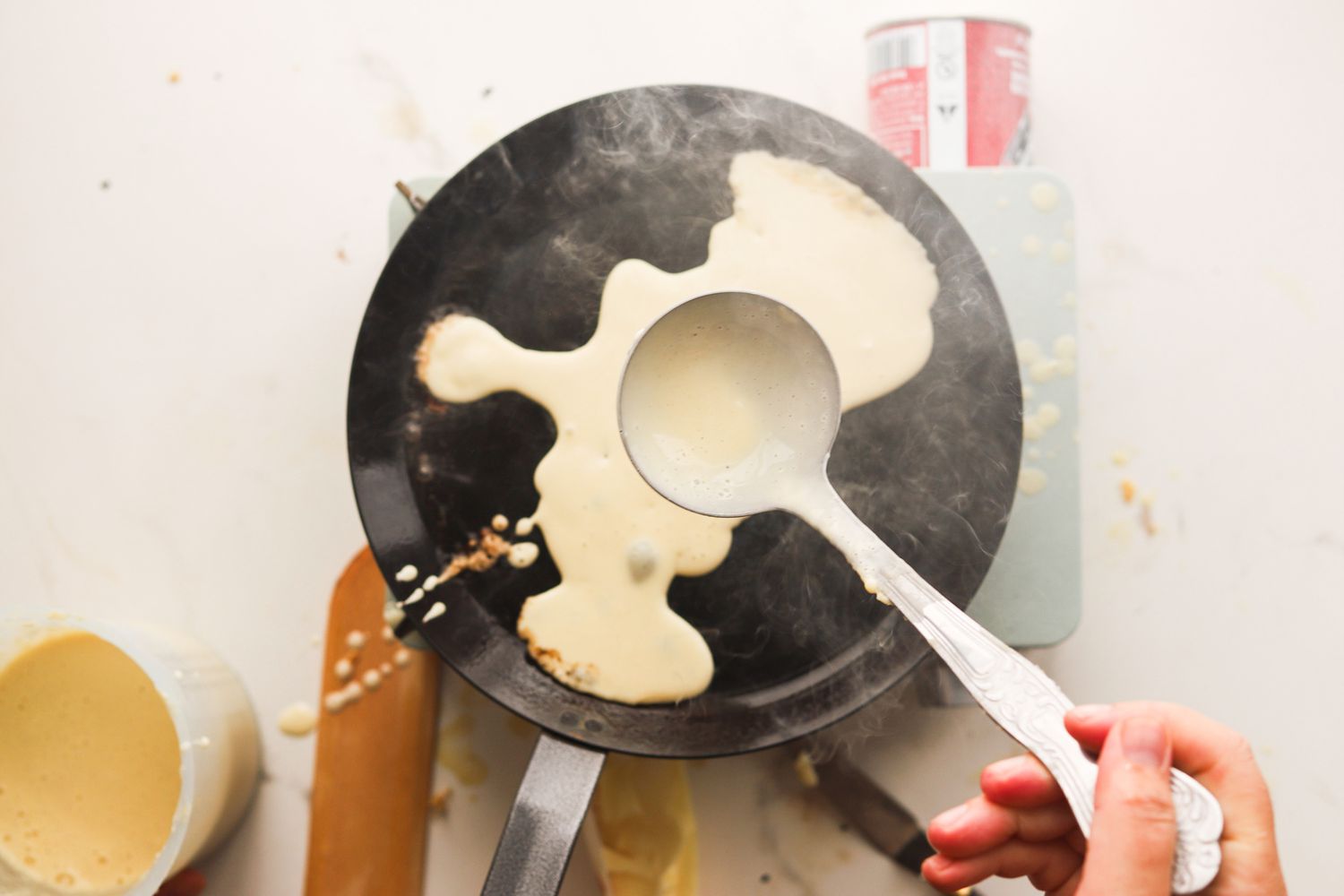 A person ladling crepe batter onto a crepe pan.