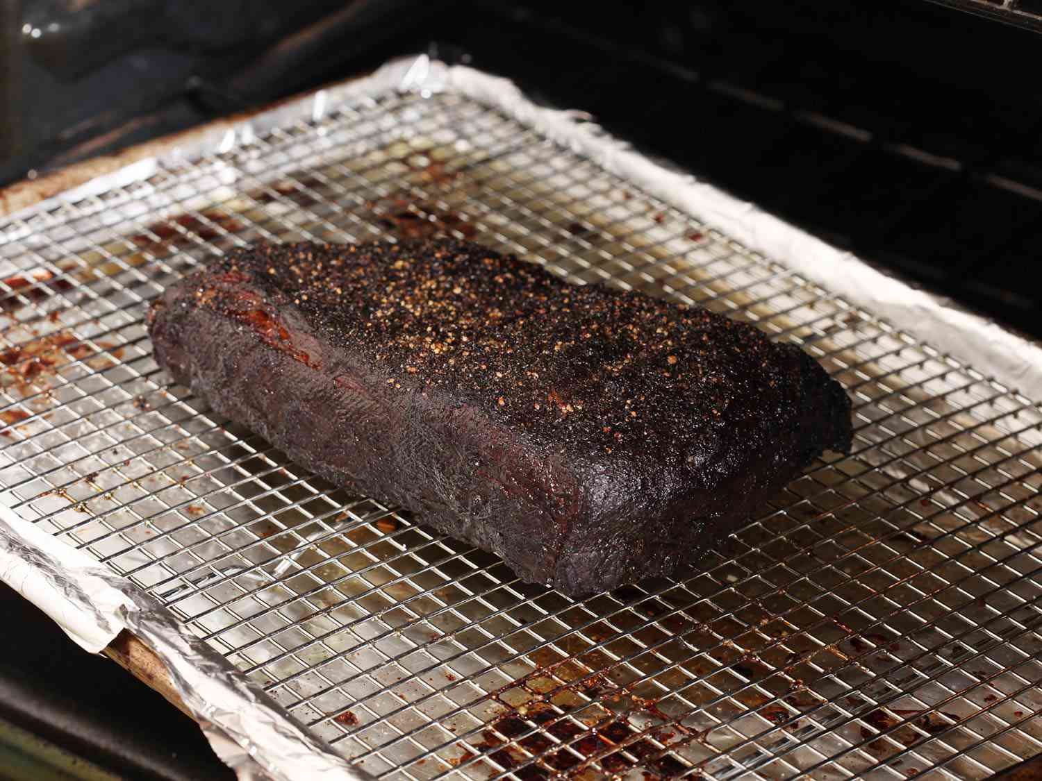 Hunk of brisket with dark crust resting on wire rack over a baking sheet. 