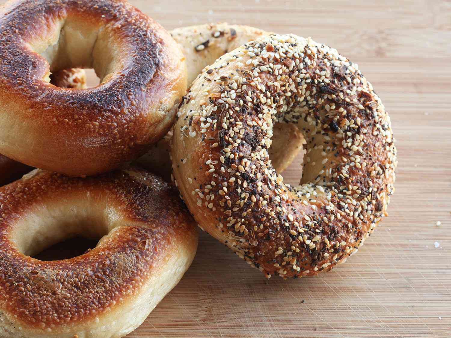Four assorted bagels on a wood countertop. 