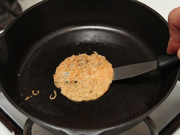 Lifting a golden crispy melted cheese round off the bottom of a cast iron skillet with a thin metal spatula.