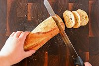 Person slicing bread with Dexter-Russell Basics 10-Inch Bread Knife With Black Polypropylene Handle