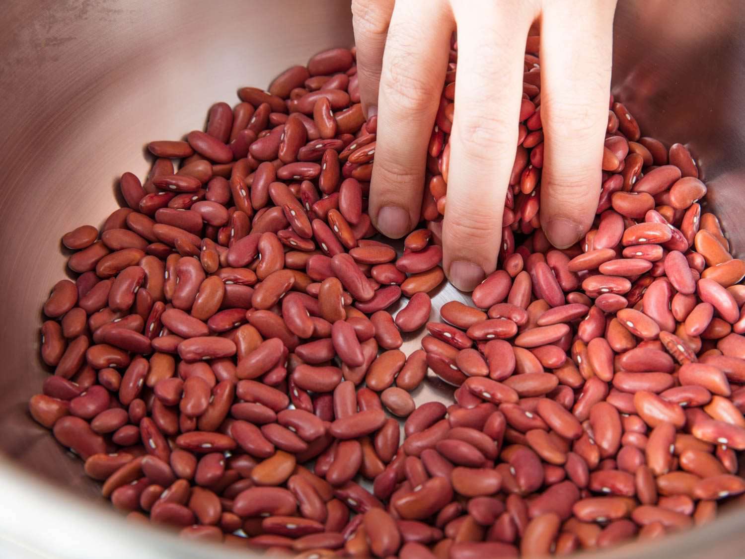 Hand picking through a bowl filled with dried kidney beans.