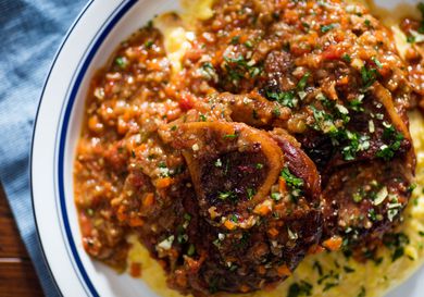 Close up photograph of a plate of osso buco and risotto alla milanese, garnished with gremolata.