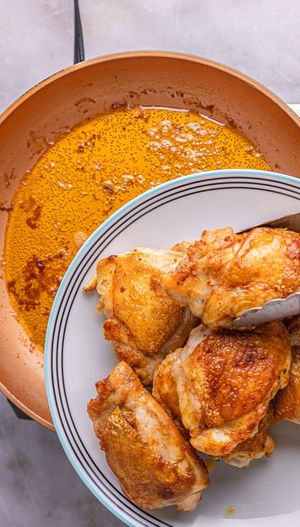 A plate with cooked chicken thighs being held above a copper pan