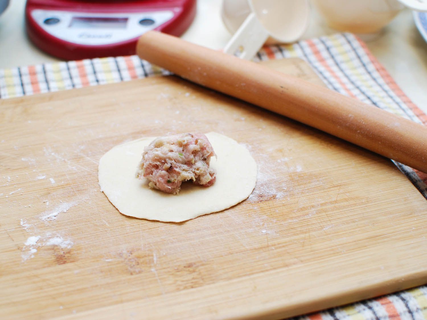 A rolled out round of sheng jian bao dough is mounded with filling.