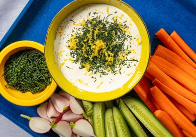 Whipped cottage cheese topped with fresh herbs and lemon zest next to raw vegetables.