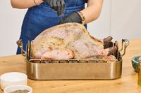A person seasoning a KellyBronze Turkey in a roasting pan