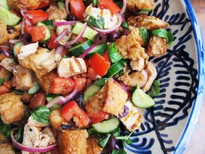 A close up of panzanella salad with grilled chicken, grilled bread, and lots of vegetables.