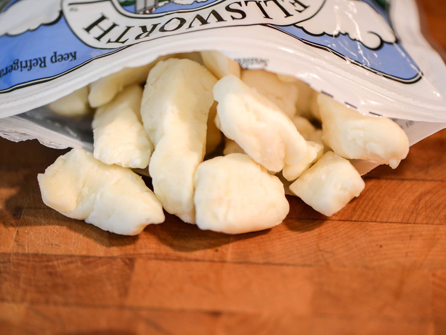 Cheese curds overflowing a bag on a wooden cutting board. 