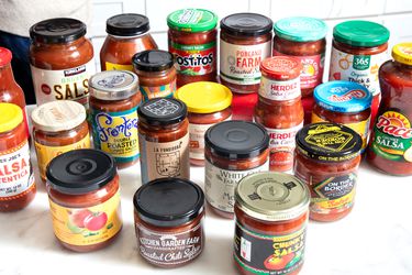 A collection of various salsa jars displayed on a white counter, showcasing different brands and types of salsas