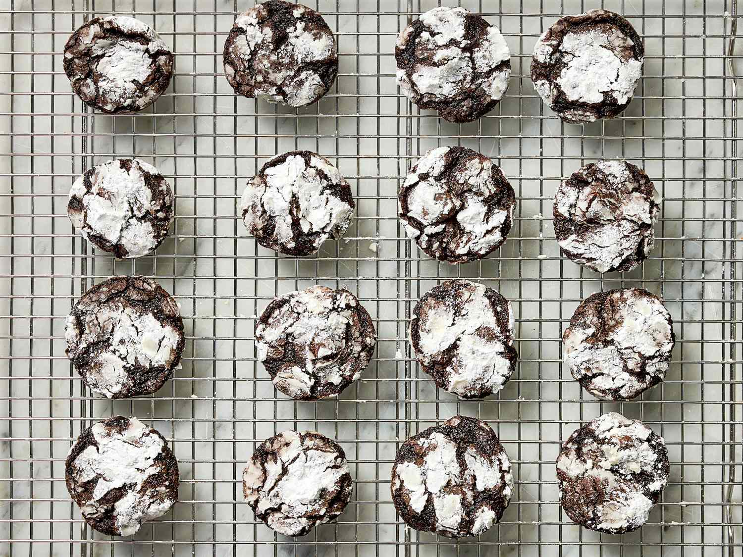 Rows of chocolate crinkle cookies topped with powdered sugar on a wire rack