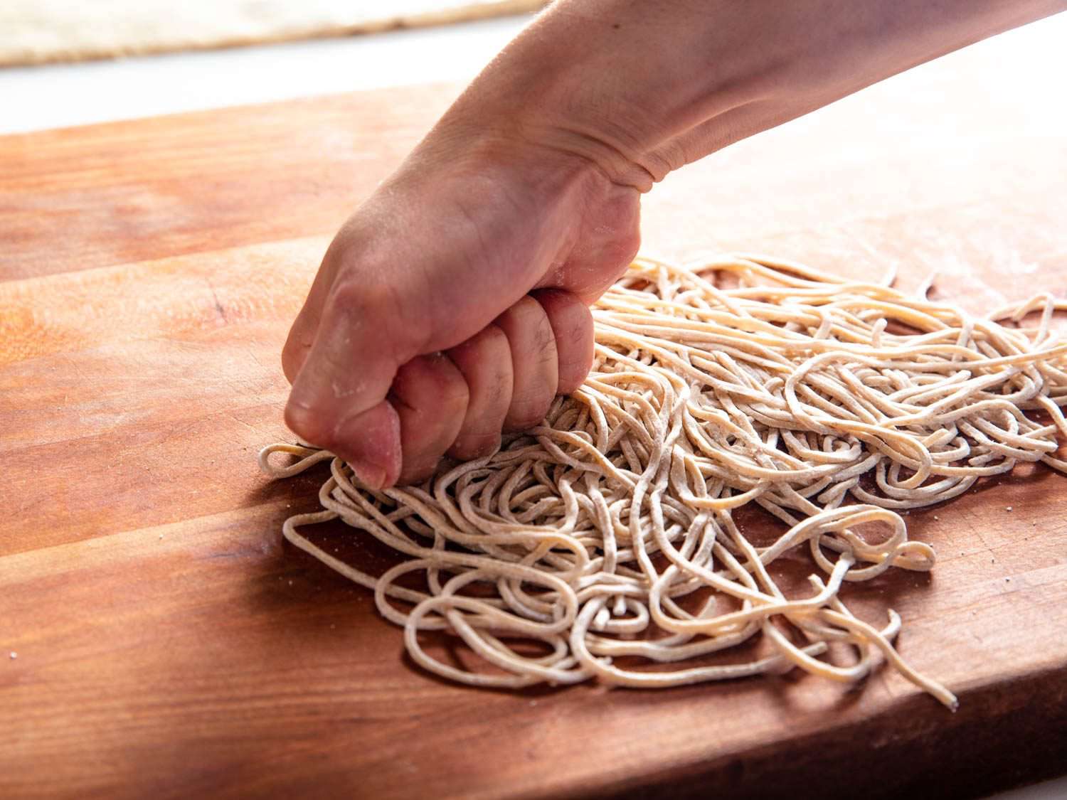 Photo of a fist compressing fresh noodles on a cutting board to create temomi noodles