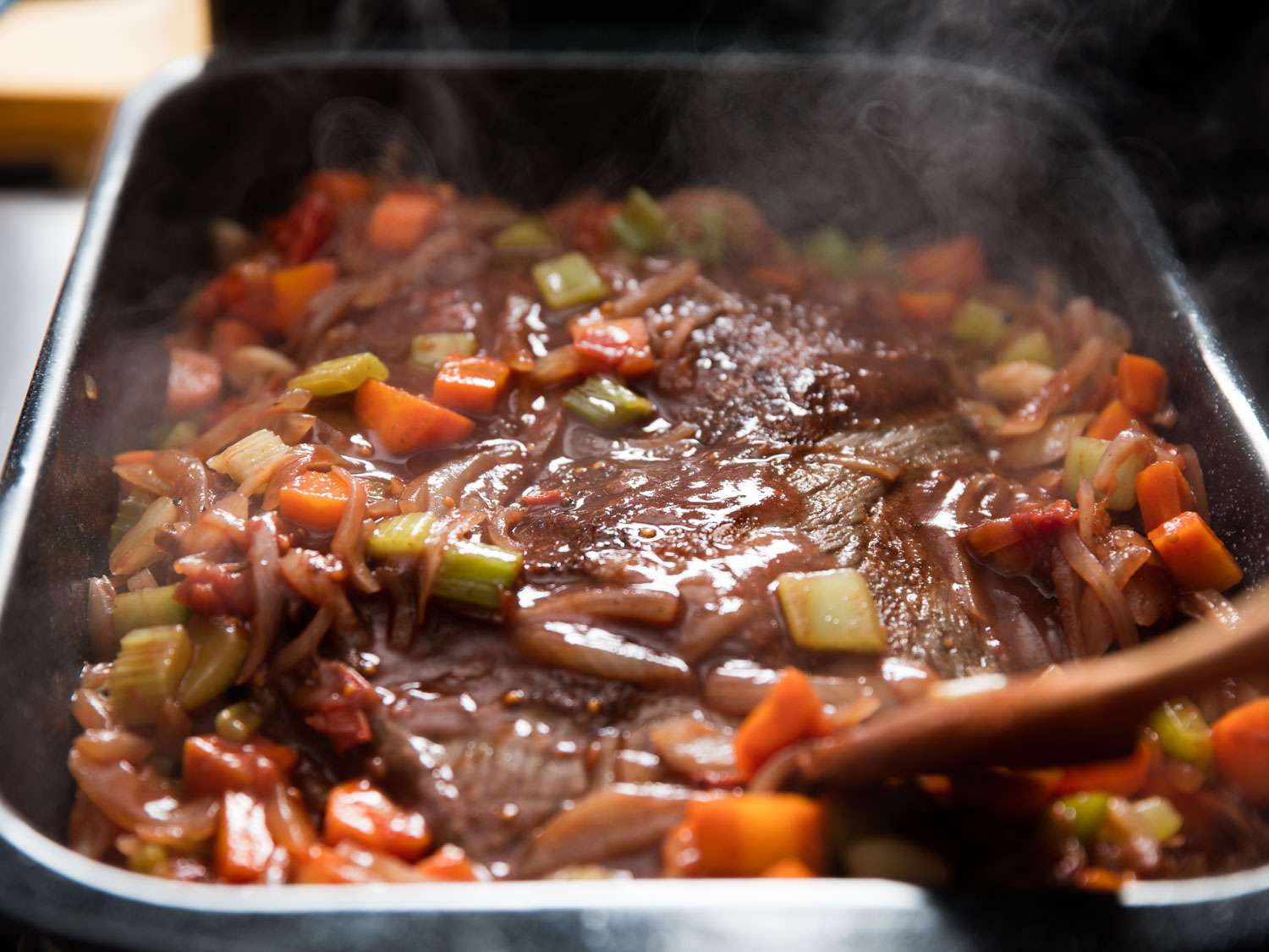 Braised brisket in a roasting pan with soft-cooked carrots and onions
