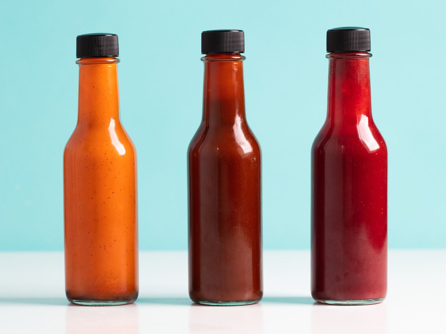 Three different flavored fermented hot sauces in glass bottles.