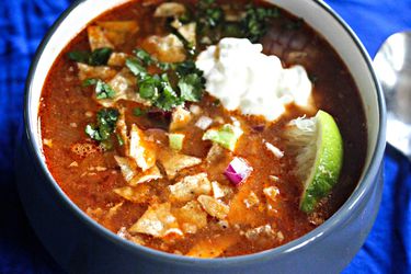 A bowl of slow-cooker chicken tortilla soup, topped with cilantro, avocado, sour cream, red onion, and lime.
