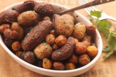 An oval white bowl filled with crispy, herb-flecked roasted potatoes.