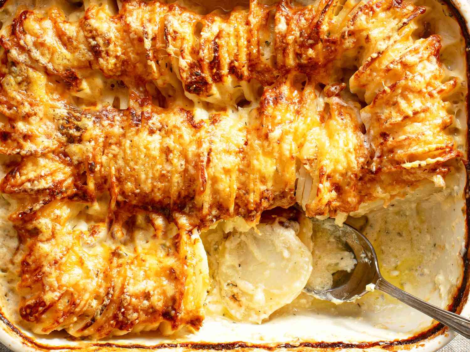 A close-up of browned Hasselback potatoes being served with a spoon.