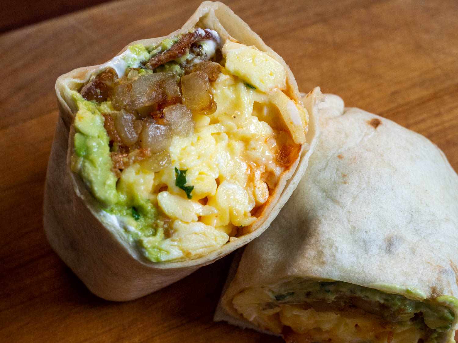 Closeup of a bacon, egg, and cheese breakfast burrito, cut in half and propped up on itself to show off the contents of the burrito to the camera.