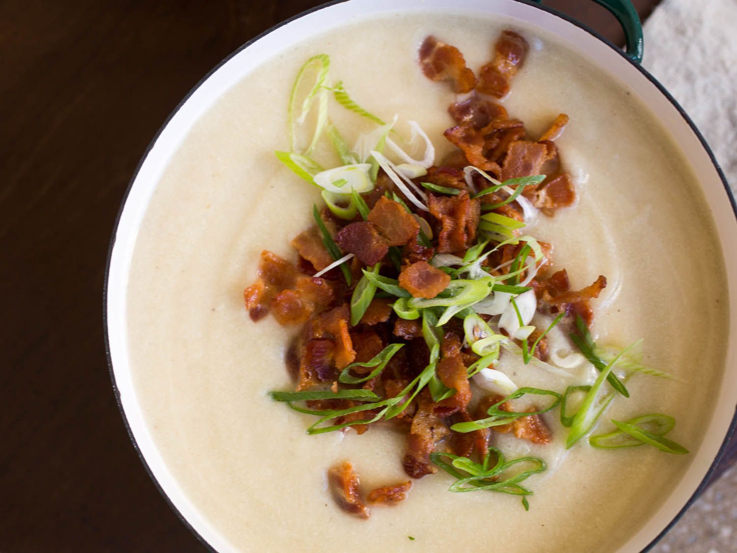 Overhead shot of a bowl of creamy cauliflower soup topped with bacon and scallions.
