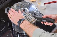 A person touches the lid of the IMUSA 7 Quart Stovetop Aluminum Pressure Cooker