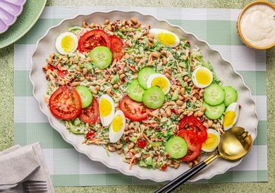 A platter of Nigerian salad topped with sliced eggs cucumbers and tomatoes displayed on a table with cutlery