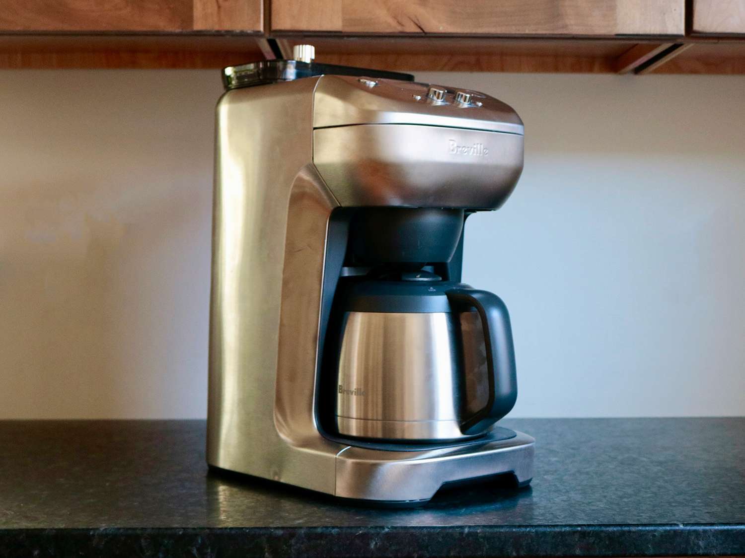 A coffee maker with a built in grinder sits on a counter with a white background