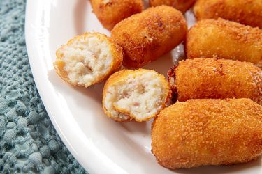 Plate of croquetas with one broken open showing the filling inside