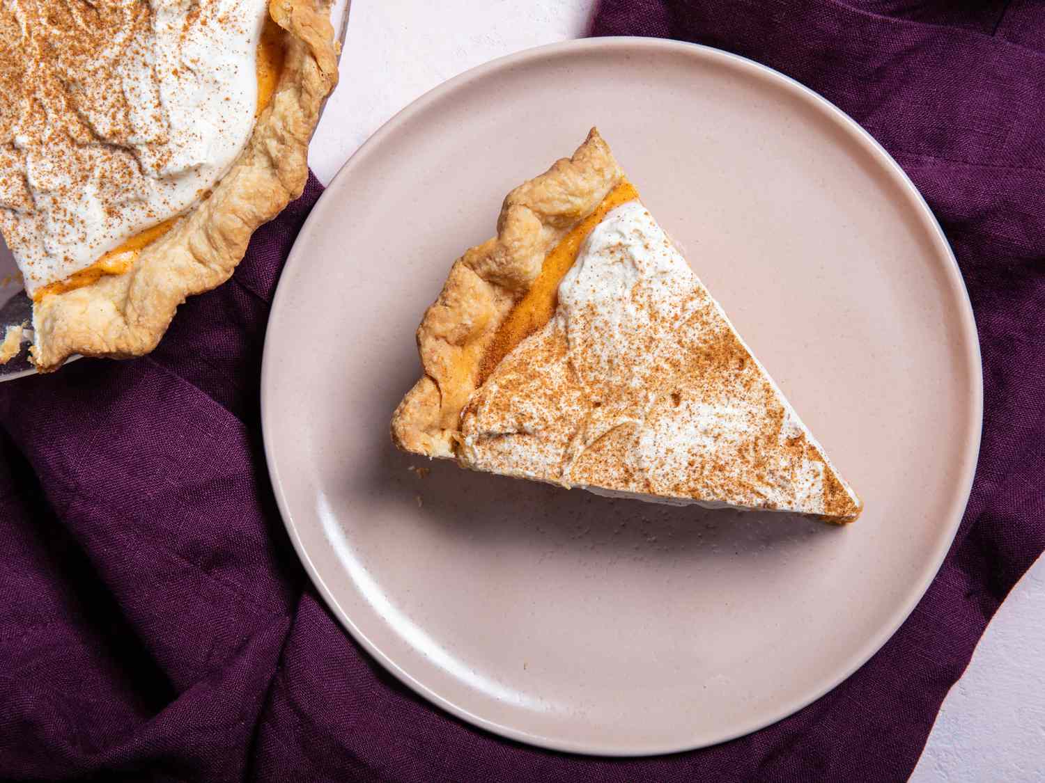 Slice of pumpkin chiffon pie on a serving plate next to pie plate with pumpkin chiffon pie