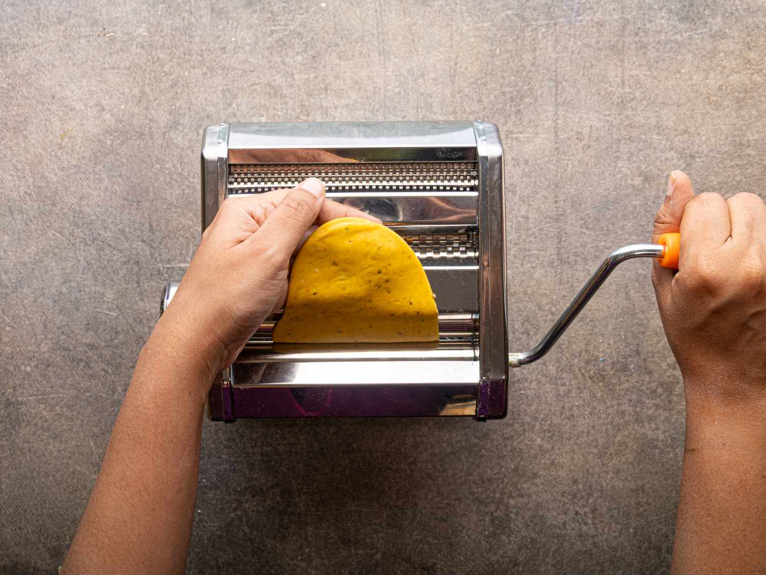 A person using a handcranked machine to press dough into a flat shape
