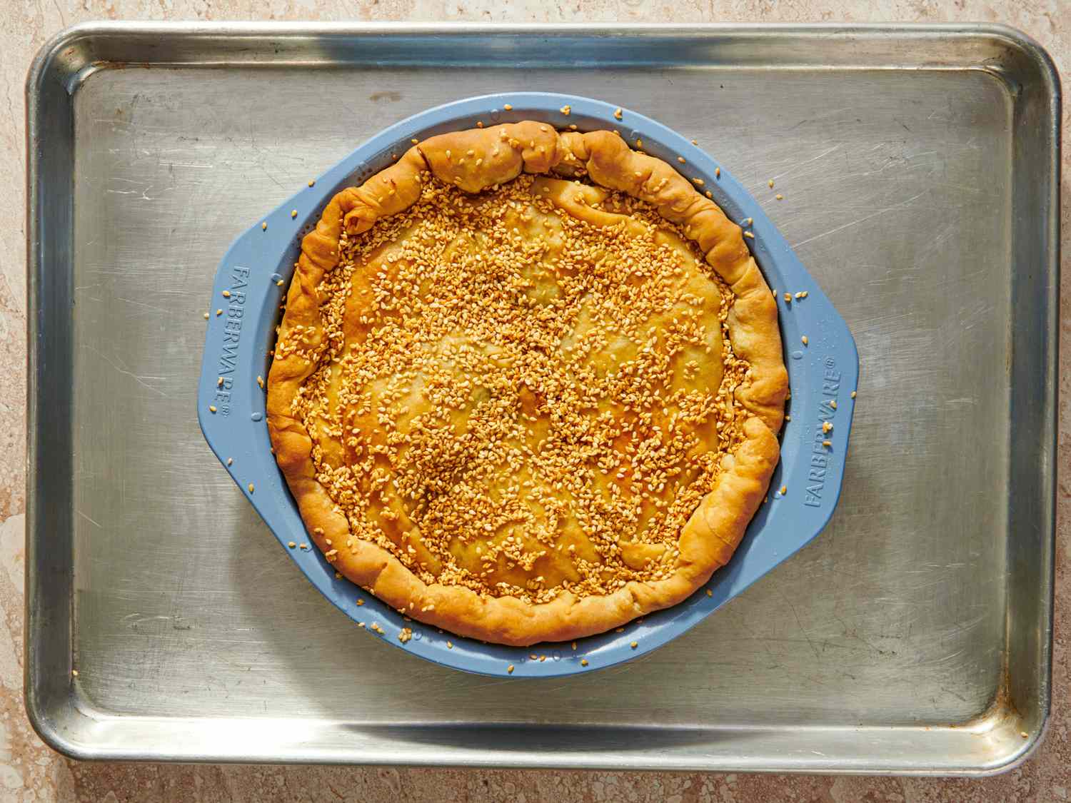 A baked pie with a sesame seed topping in a round silicone pan on a baking tray