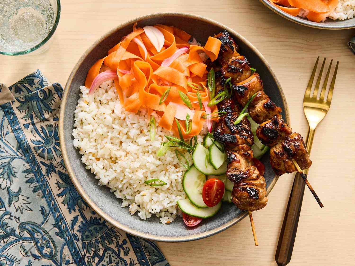 carrot ribbons in a bowl with rice, cucumber and chicken skewers 