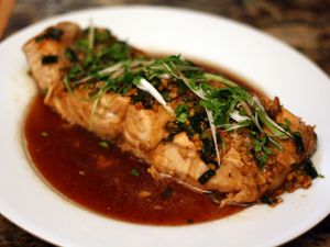 A steamed salmon fillet garnished with scallions and sitting in a flavorful sauce.