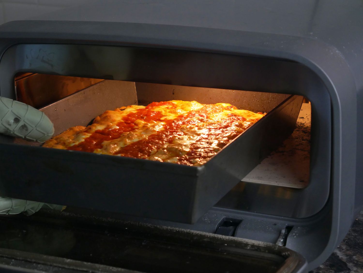 a person removing a pan pizza from an indoor pizza oven