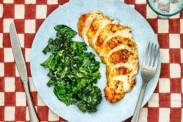 Sliced chicken breast on a plate with sautéed kale.