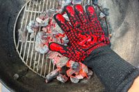 A person hold their hand to hot coals while wearing the Comsmart BBQ Gloves