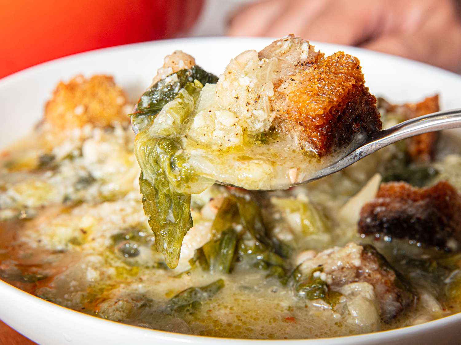A spoonful of soup with greens beans and croutons lifted from a bowl