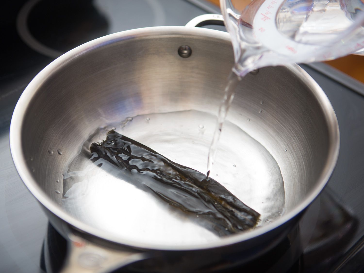 Pouring water over a piece of dried kombu in a pan.