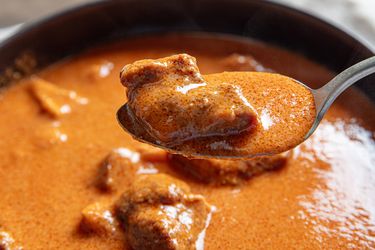 A closeup of a spoon holding a piece of meat in a creamy soup with the bowl of soup visible in the background