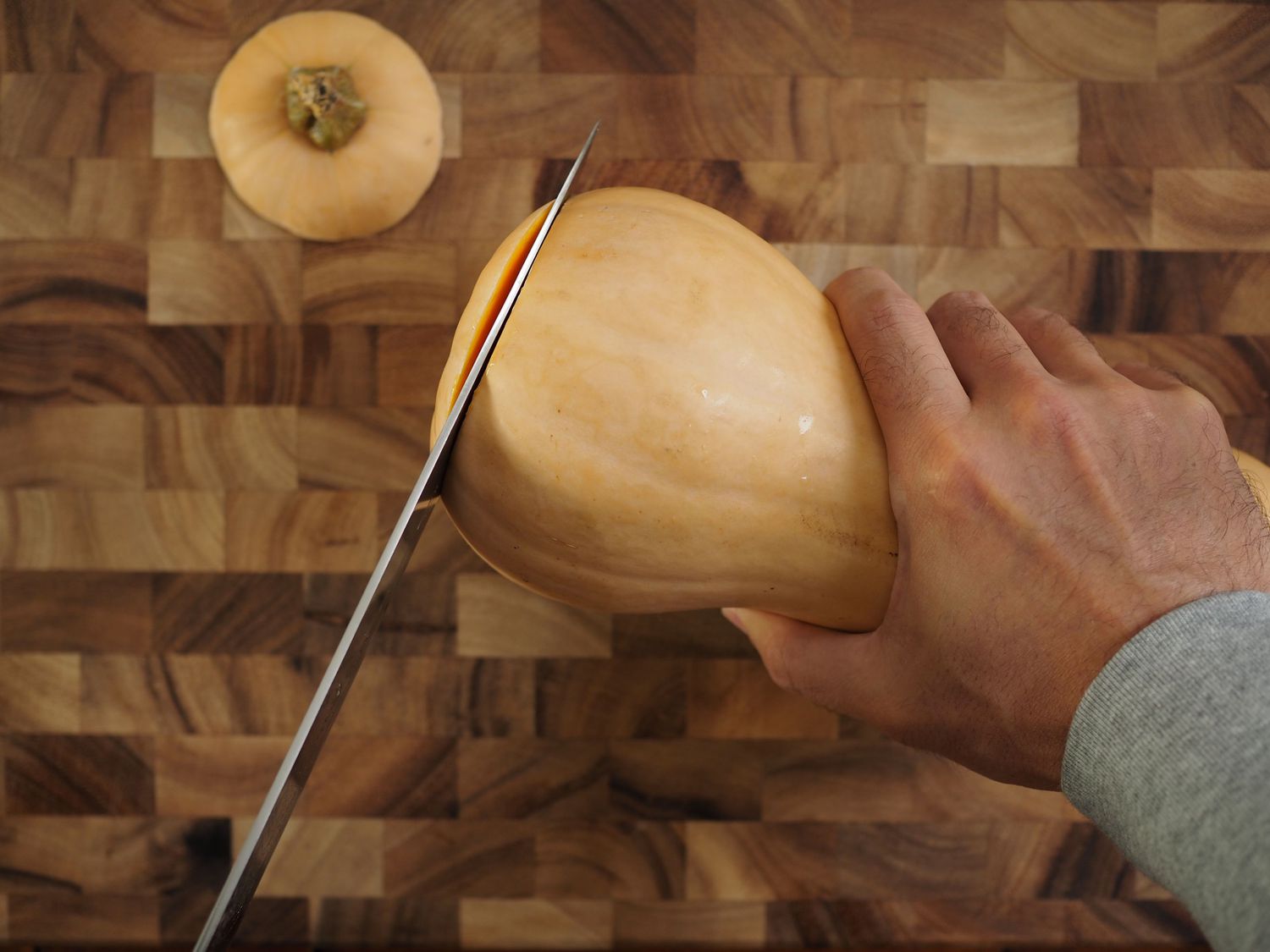 A knife trimming the bottom off of a butternut squash, with a hand firmly gripping the squash by the nedk.