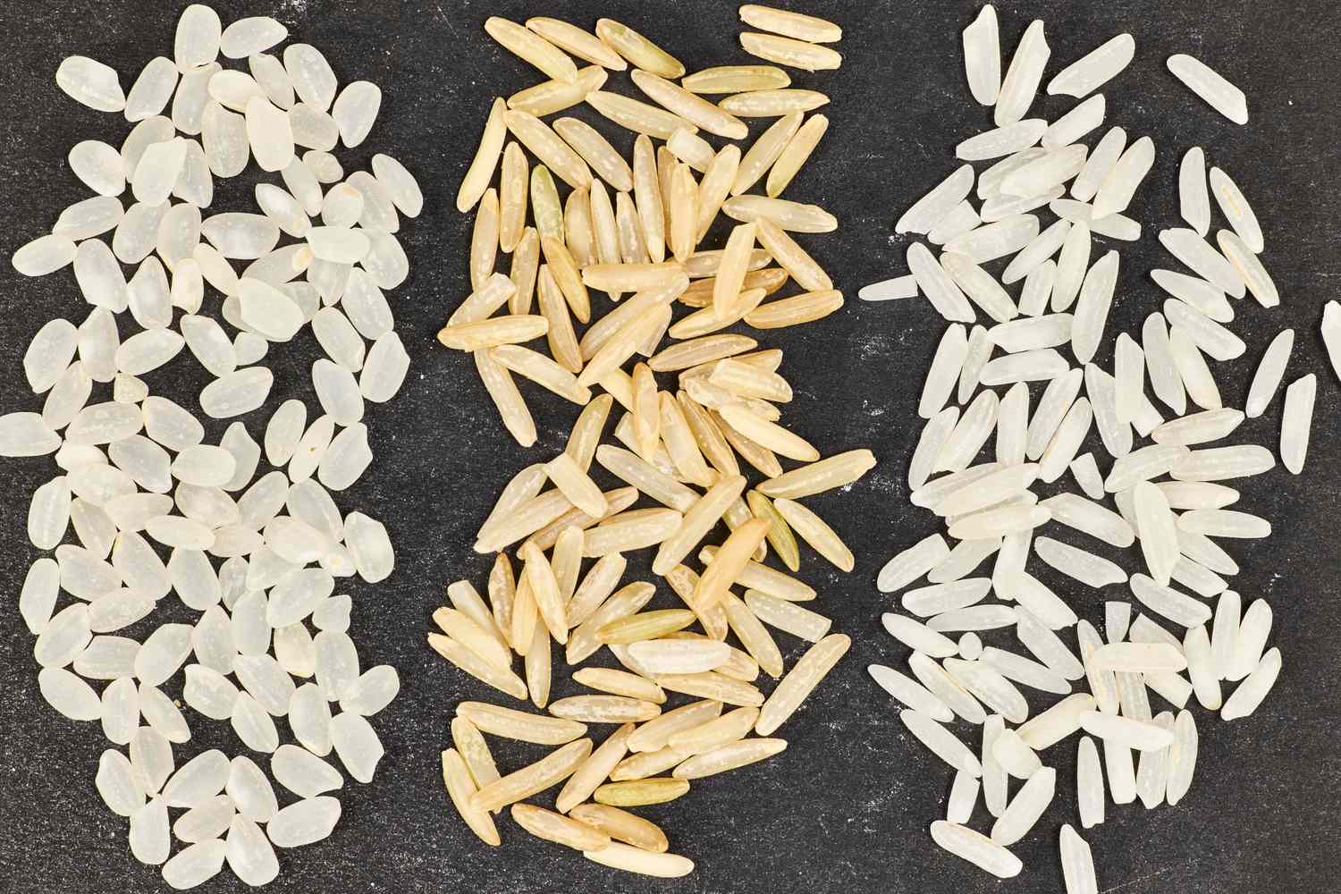 Three different types of uncooked rice on a black background