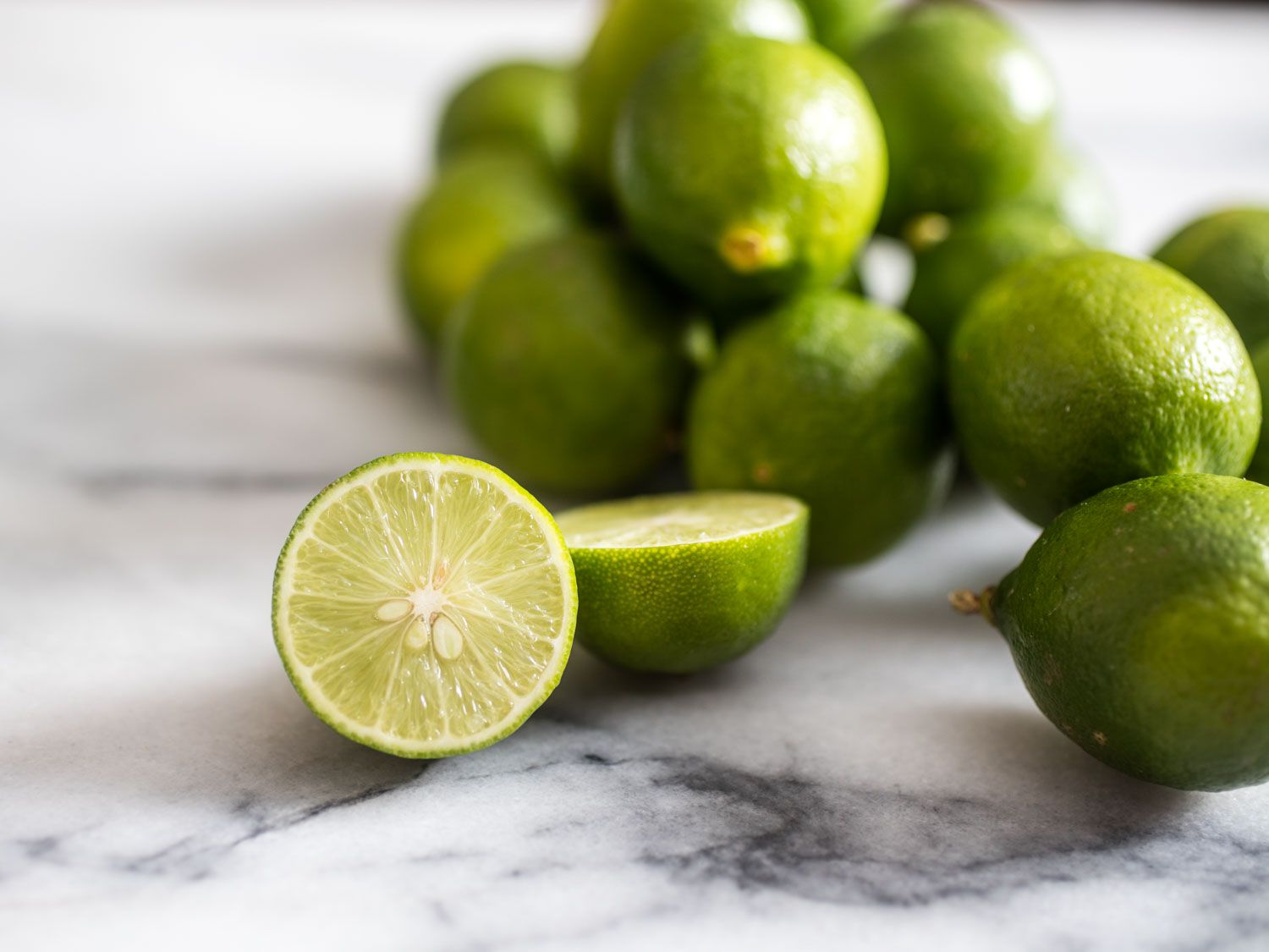 Key limes on a marble countertop. One lime is cut in half. 