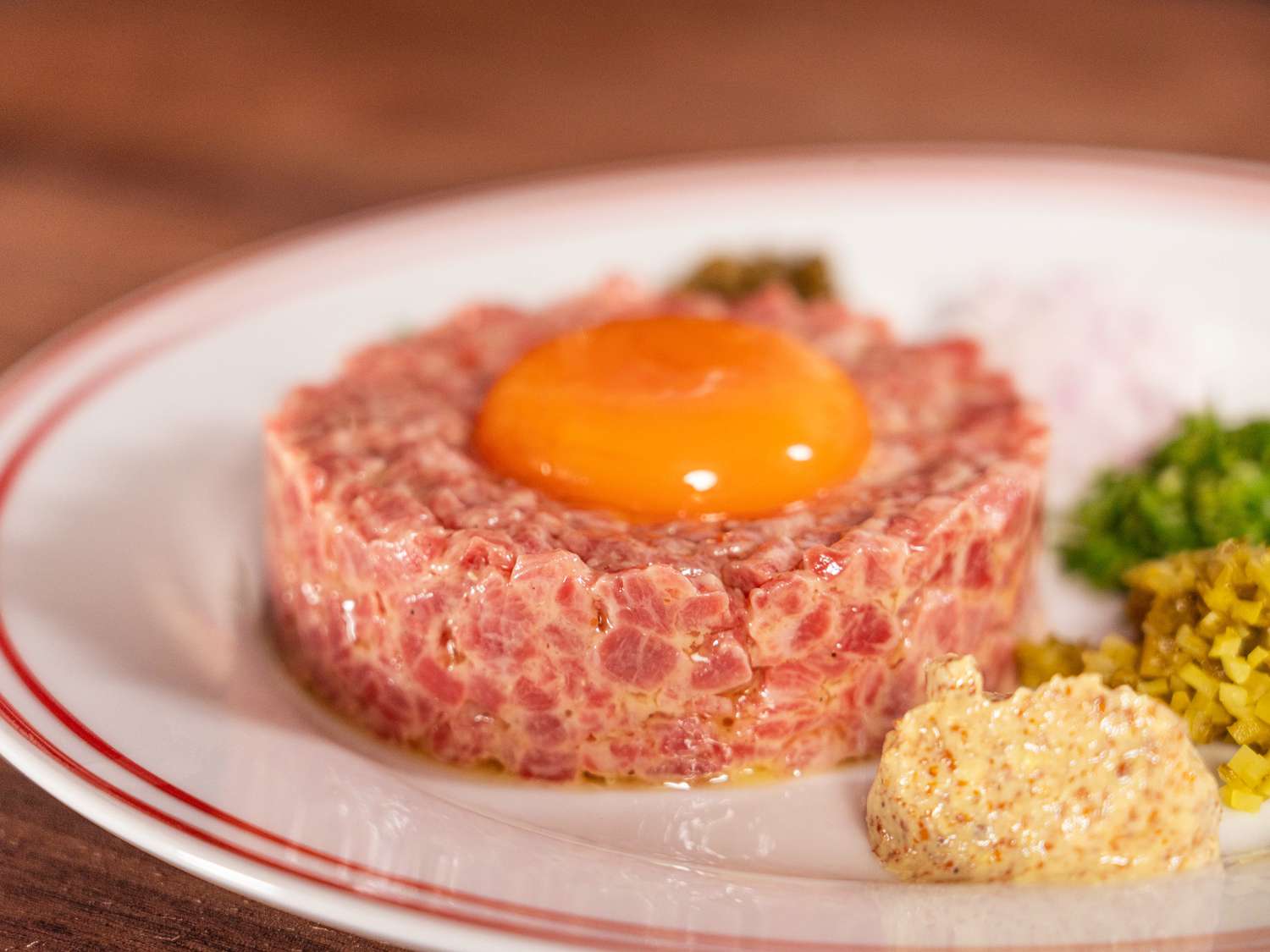 beef tartar on a dish with a raw egg dropped into form, and capers, onions, mustard and herbs stacked around it on a white plate 