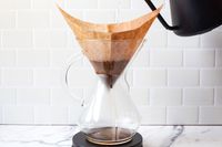 Pour-over coffee being brewed in a glass coffee maker with a paper filter and hot water poured from a kettle